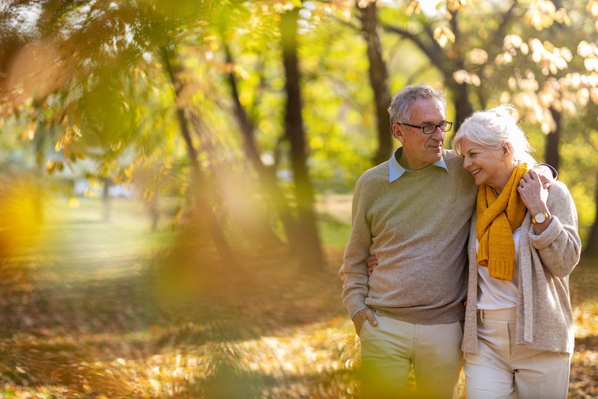 Older couple walking together through a sunlit autumn park